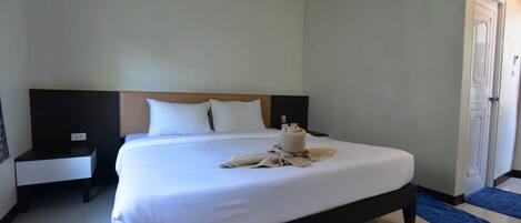 A neatly made bed with white linens and a towel, a bedside table with a lamp, and a door with a mat.