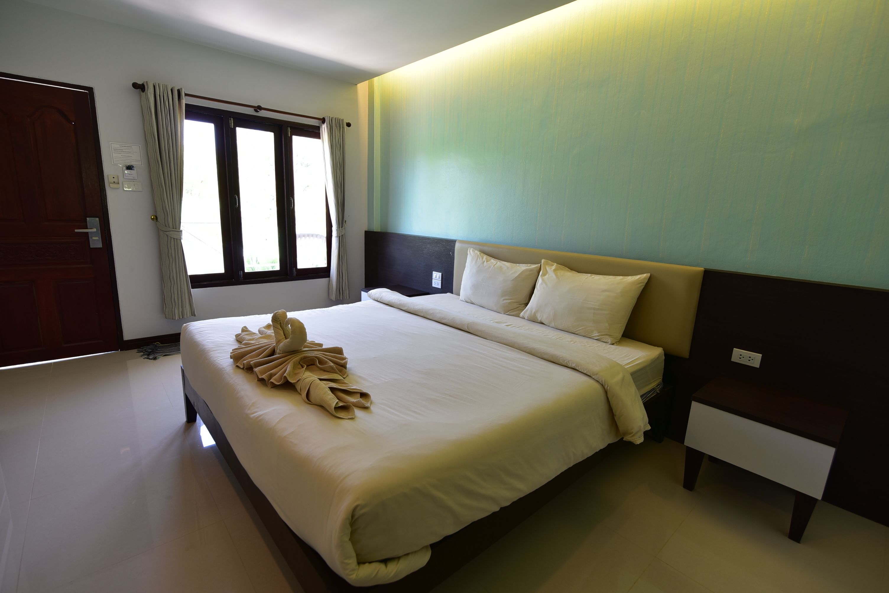 A hotel room with a large bed, a bedside table, a window with curtains, and a door.