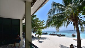 A beach view from a balcony with a railing, palm trees, and boats on the water.
