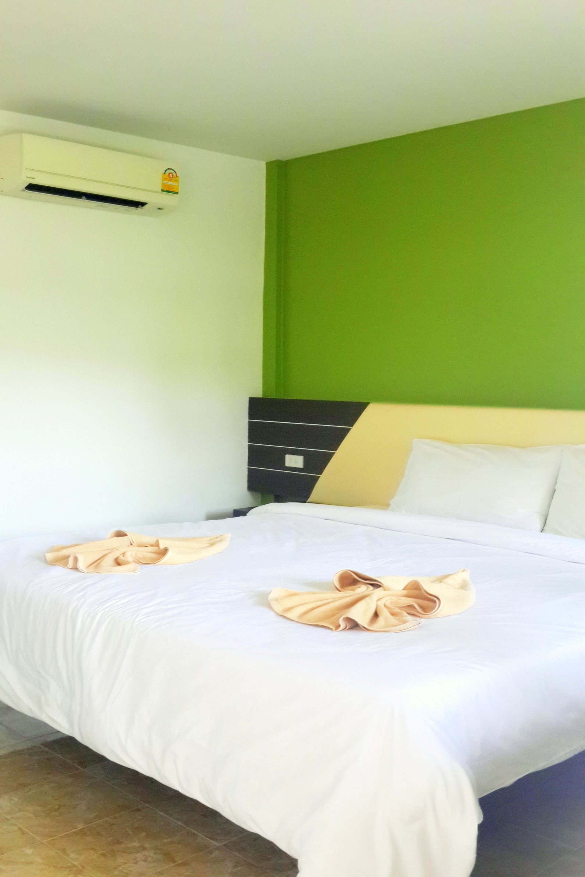 A hotel room with a bed, green walls, a black headboard, and an air conditioning unit.