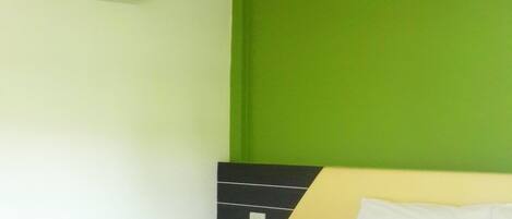 A hotel room with a bed, green walls, a black headboard, and an air conditioning unit.