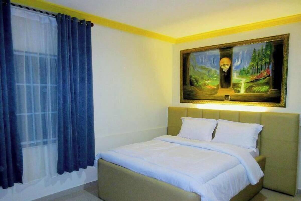 Un dormitorio con una cama, un cuadro y una ventana con cortinas.