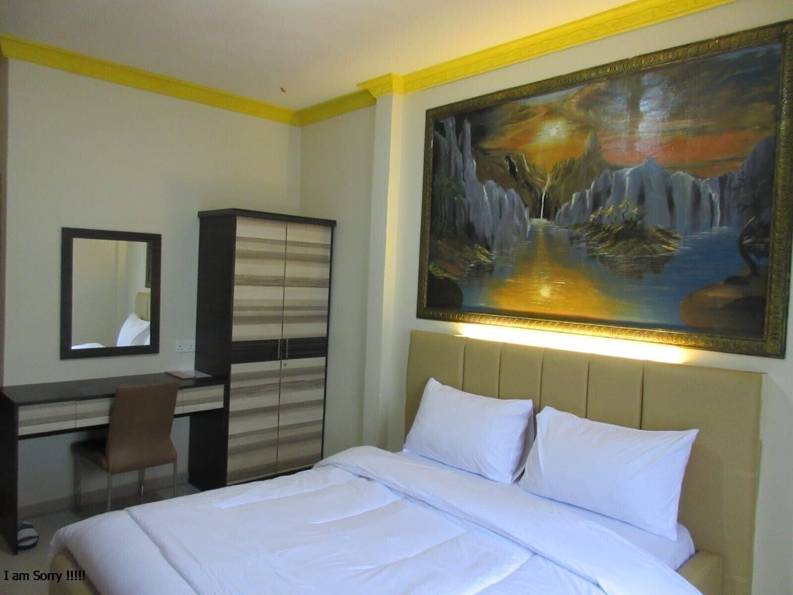 A hotel room with a bed, a desk, a chair, a wardrobe, and a large painting on the wall.
