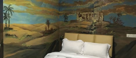 A bed with white bedding in a room with a mural depicting a desert landscape and palm trees.