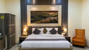 Een slaapkamer met een groot bed, twee nachtkastjes met lampen, een stoel, een garderobe en een groot schilderij aan de muur.