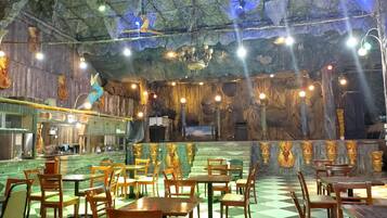 A restaurant with a checkered floor, wooden tables and chairs, and a cave-like interior with stone walls and hanging lights.