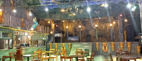 Ein Restaurant mit Schachbrettboden, Holztischen und -stühlen und einem grottenartigen Innenraum mit Steinwänden und hängenden Lampen.