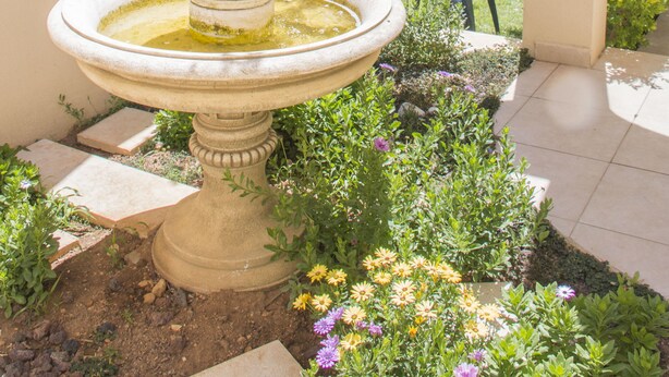 Un jardin avec une fontaine, une table et des chaises sous une arche.