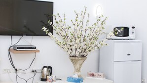 Une pièce avec un téléviseur fixé au mur, une petite table sur laquelle est posé un vase de fleurs, un four à micro-ondes et un réfrigérateur.