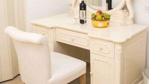 Une coiffeuse blanche avec un miroir, un flacon de parfum et un bol de fruits.