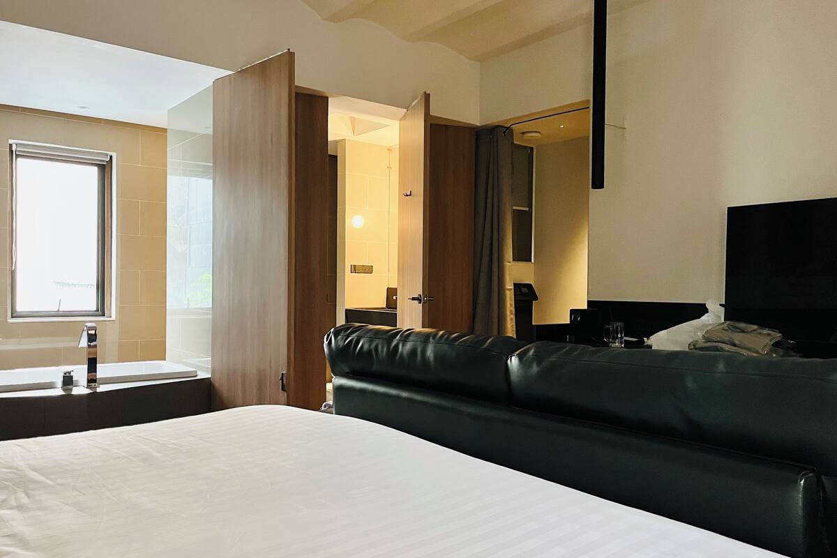 Moderni hotellihuone, jossa on suuri sänky, yöpöytä, peili ja ikkuna.