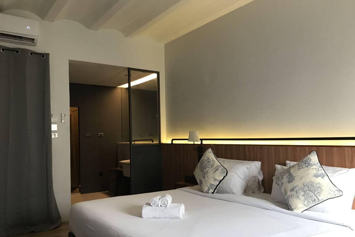 Hotellihuone, jossa on suuri sänky, peili, yöpöytä ja kylpyhuone, joka näkyy avoimesta ovesta.