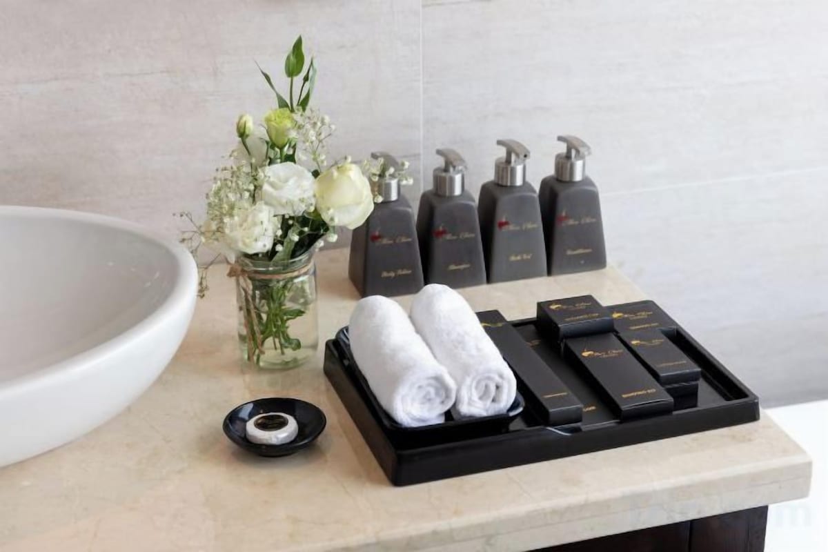 A bathroom vanity with a large sink, a vase of flowers, and a tray with rolled towels and toiletries.
