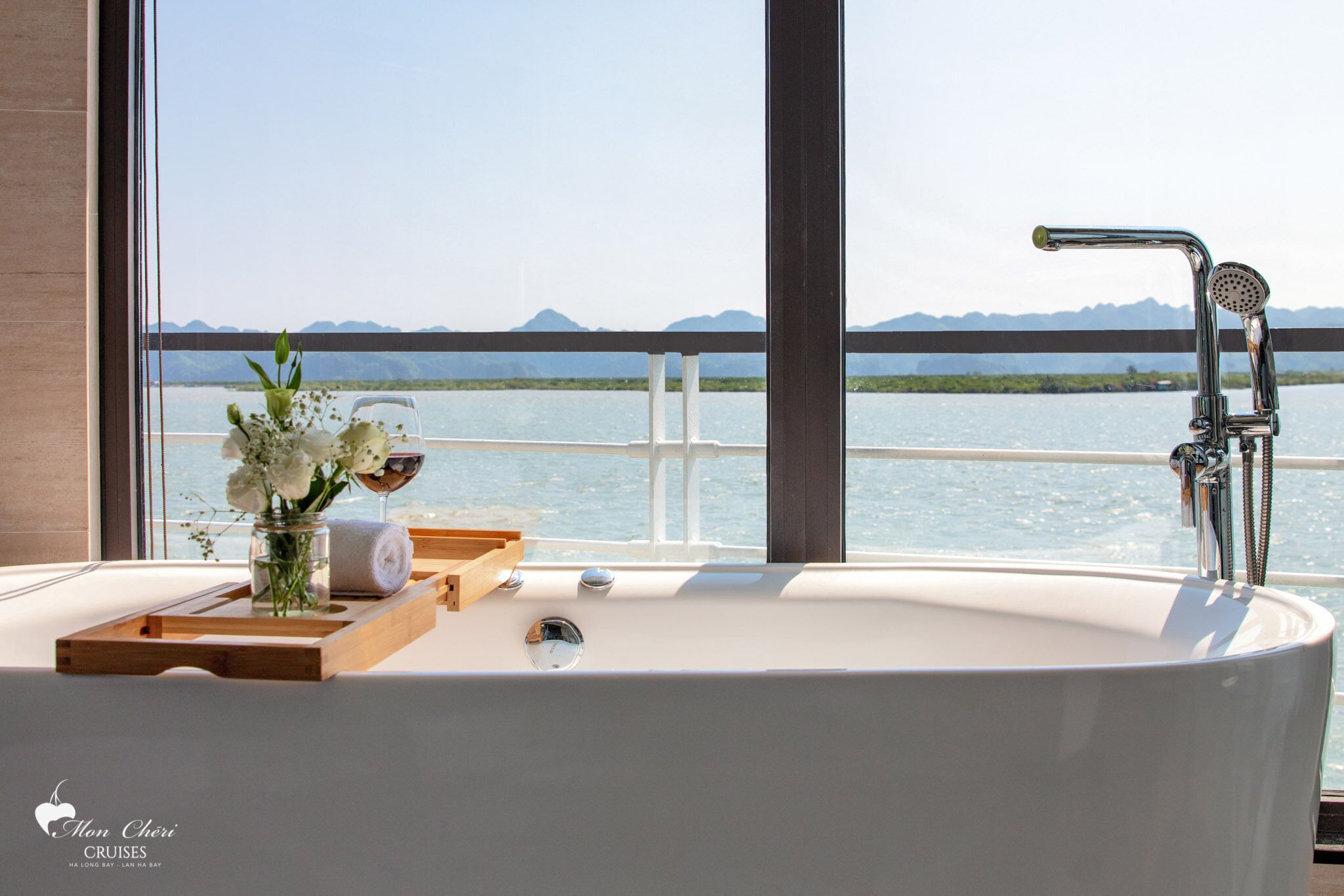 A bathroom with a bathtub, a glass shower enclosure, and a view of a body of water with mountains in the distance.