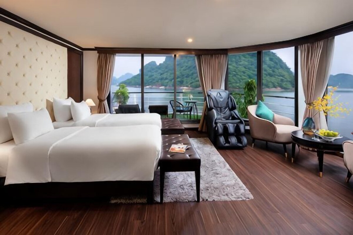 A hotel room with a large bed, a massage chair, a small table, and a view of the water.