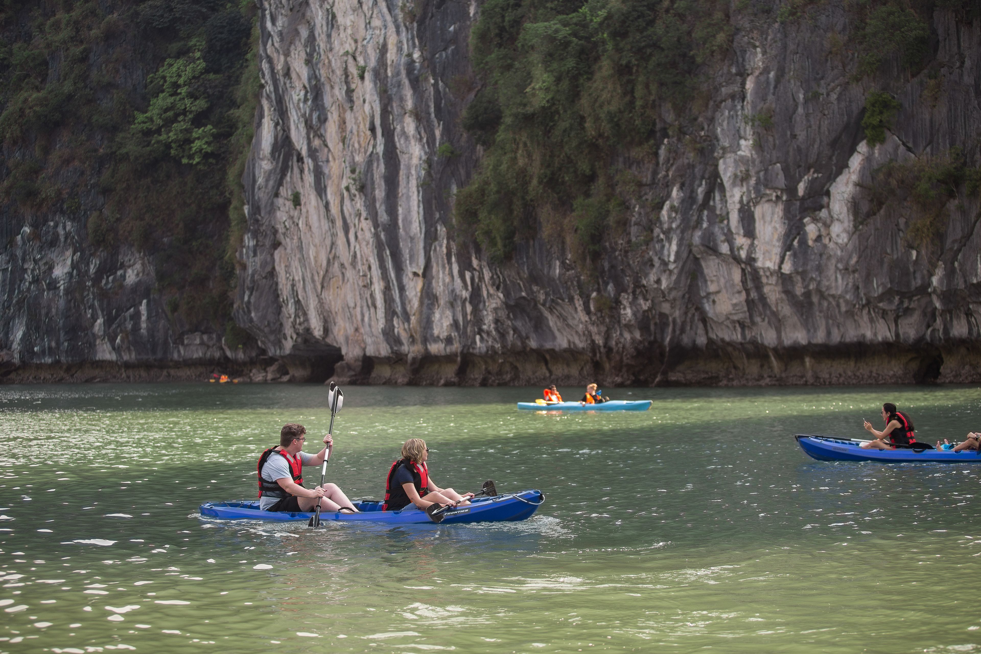 Un gruppo di persone fa kayak su un fiume calmo con ripidi dirupi sullo sfondo.