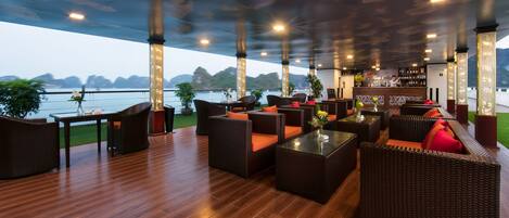 Un área de estar al aire libre techada con muebles de mimbre, un bar y vistas al agua.