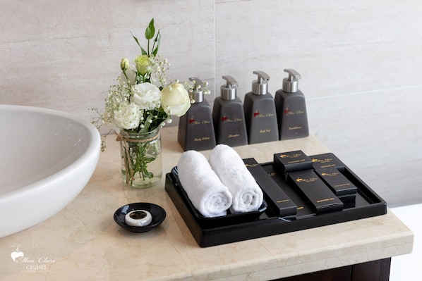 A bathroom vanity with a white sink, a vase with white flowers, and toiletries including shampoo and conditioner bottles. - Mon Chéri Cruises (Tuan Chau)