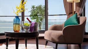 A modern room with a view of the sea, a sofa with a green cushion, a table with a vase of yellow flowers, and a lamp. - Mon Chéri Cruises (Tuan Chau)