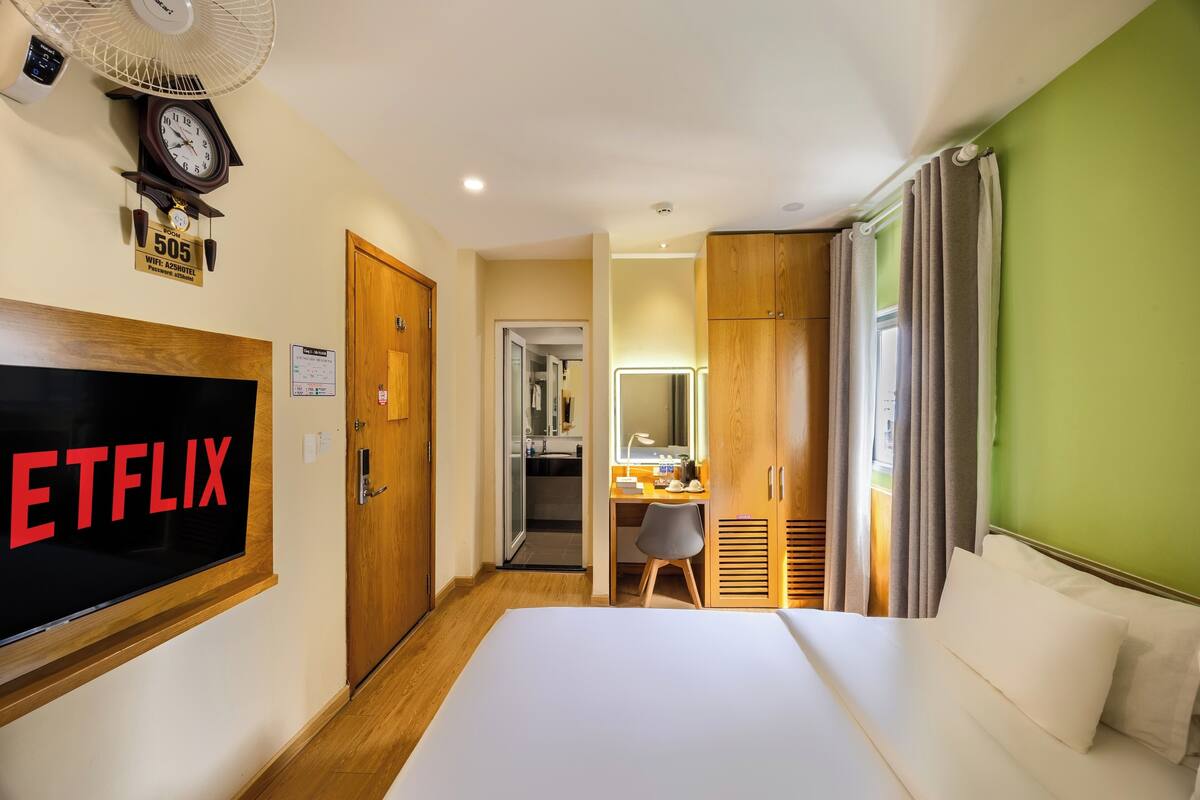 A hotel room with a bed, a desk, a mirror, a clock, and a TV displaying the Netflix logo.