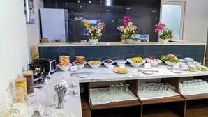 A buffet setup with various food items and beverages, a coffee machine, and decorative flowers. - A25 Premium Hotel - 142 Bui Thi Xuan (Ho Chi Minh City)