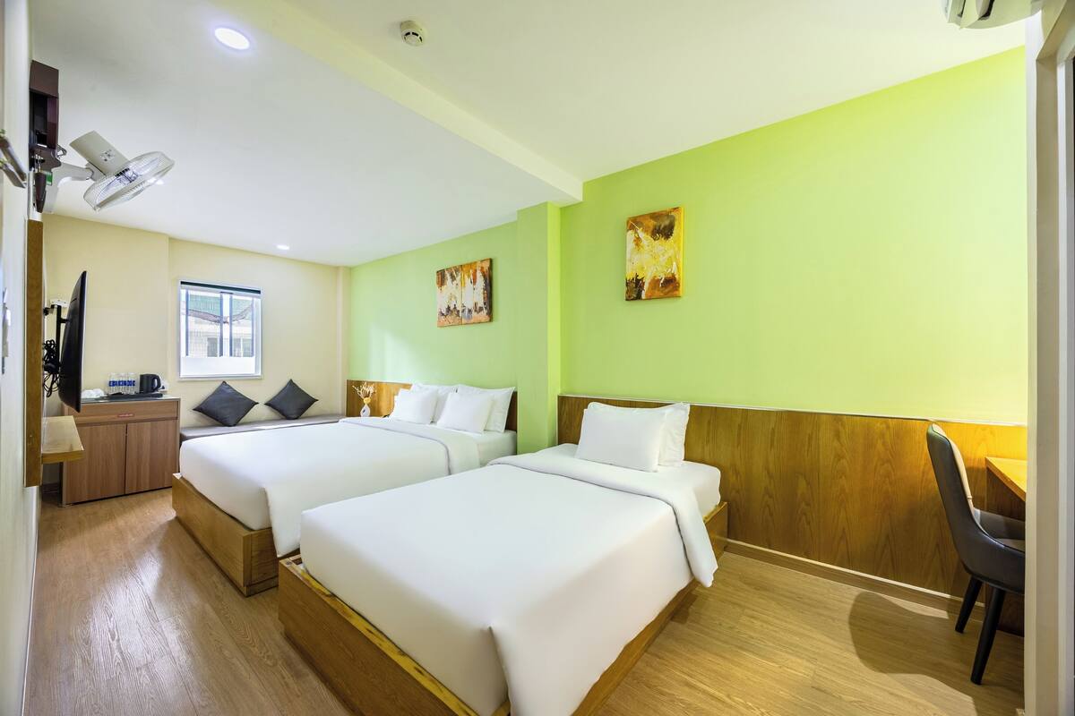 A hotel room with two beds, a desk, a chair, a TV, and artwork on the walls.