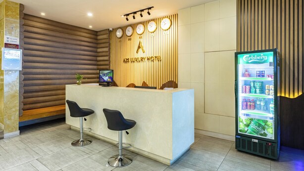 A reception area with a wooden wall, a reception desk, two black bar stools, and a Carlsberg refrigerator. - A25 Premium Hotel - 142 Bui Thi Xuan (Ho Chi Minh City)