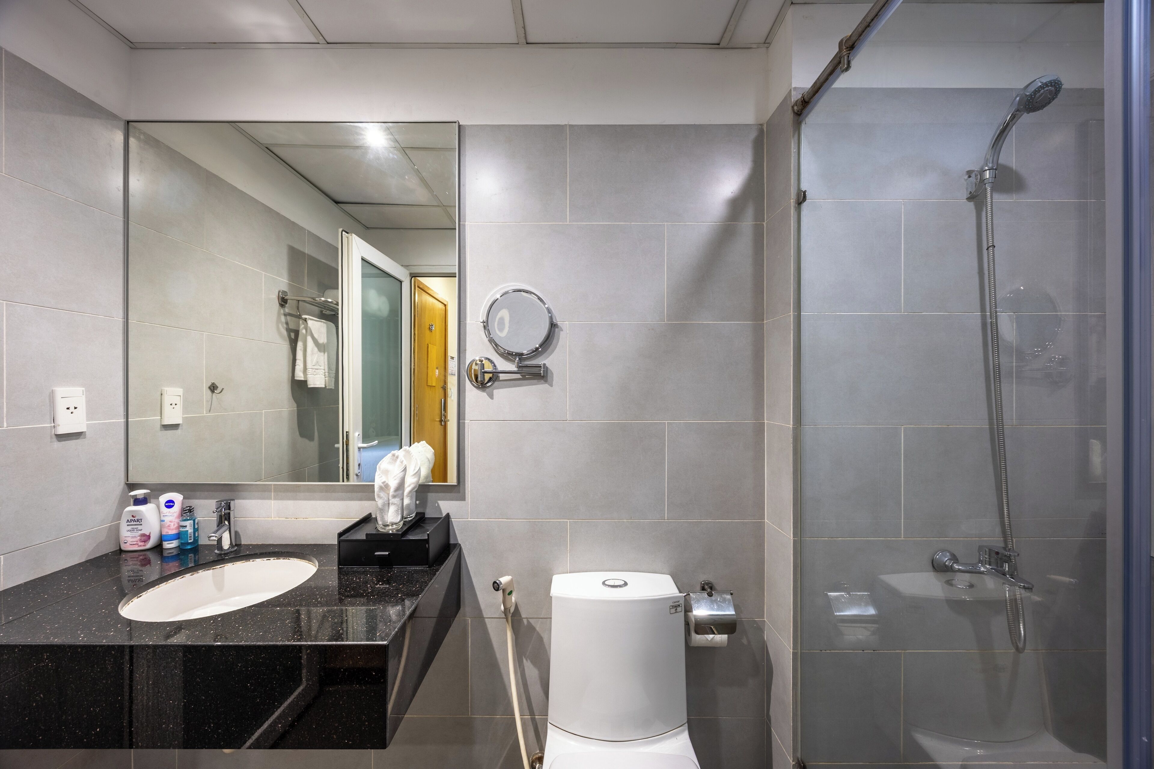A modern bathroom with a large mirror, a sink, a toilet, and a glass-enclosed shower.