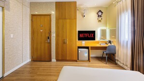 A hotel room with a wooden wardrobe, a desk with a computer and a clock, a bed, and a window with curtains. - A25 Premium Hotel - 142 Bui Thi Xuan (Ho Chi Minh City)