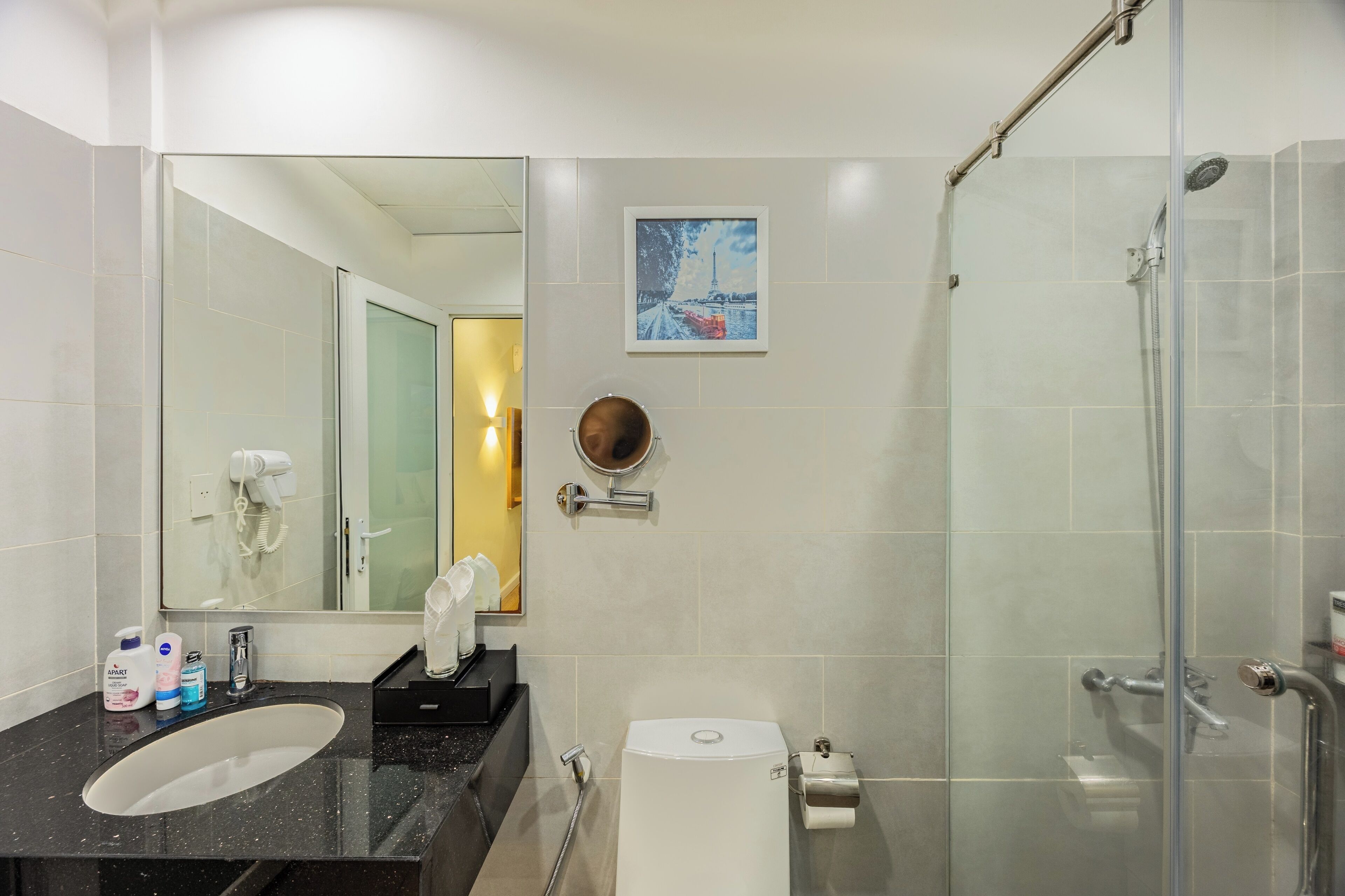 Une salle de bain moderne avec une douche à parois de verre, un lavabo doté d’accessoires de toilette et un grand miroir.