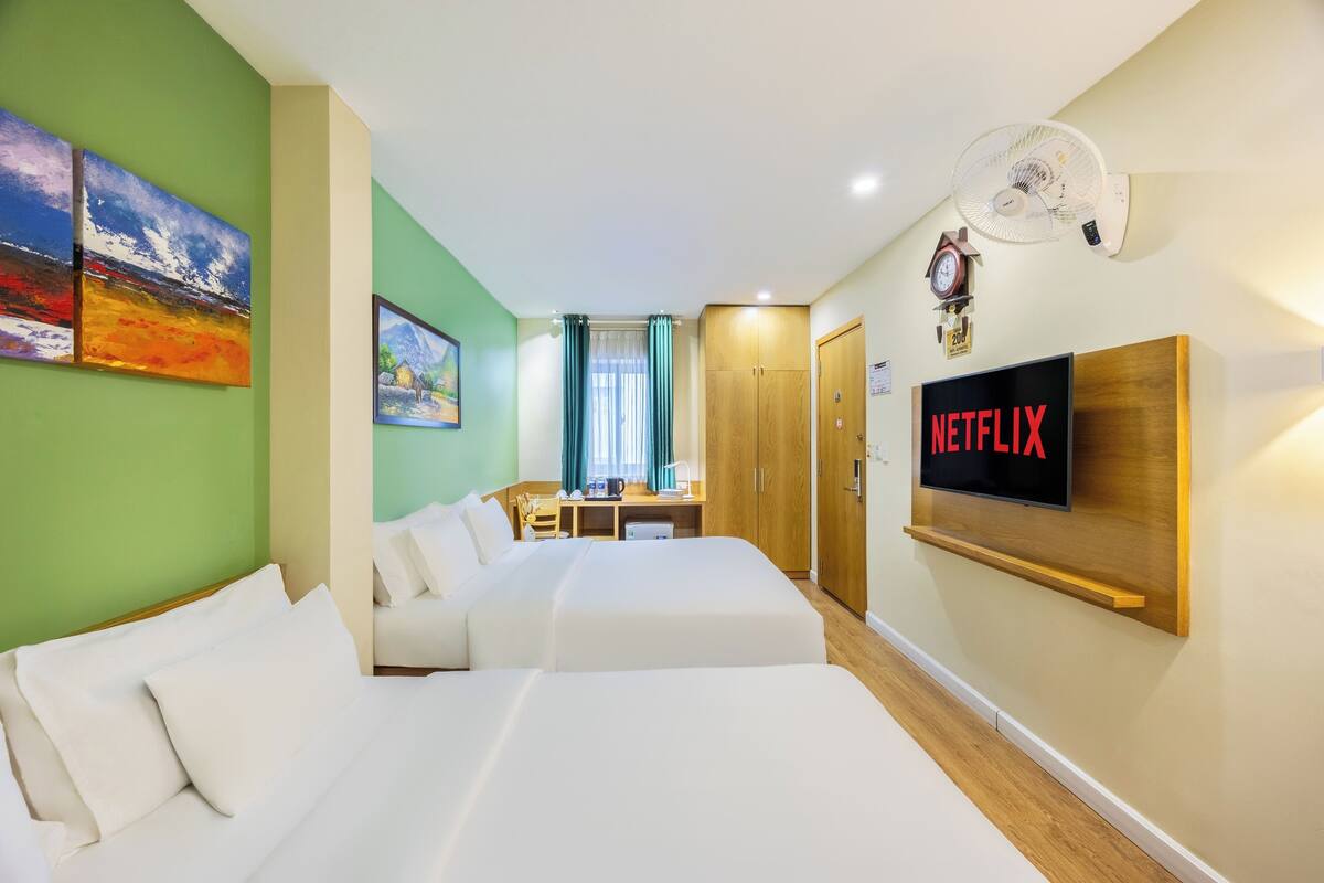 A hotel room with two beds, a desk, a TV, and artwork on the walls.