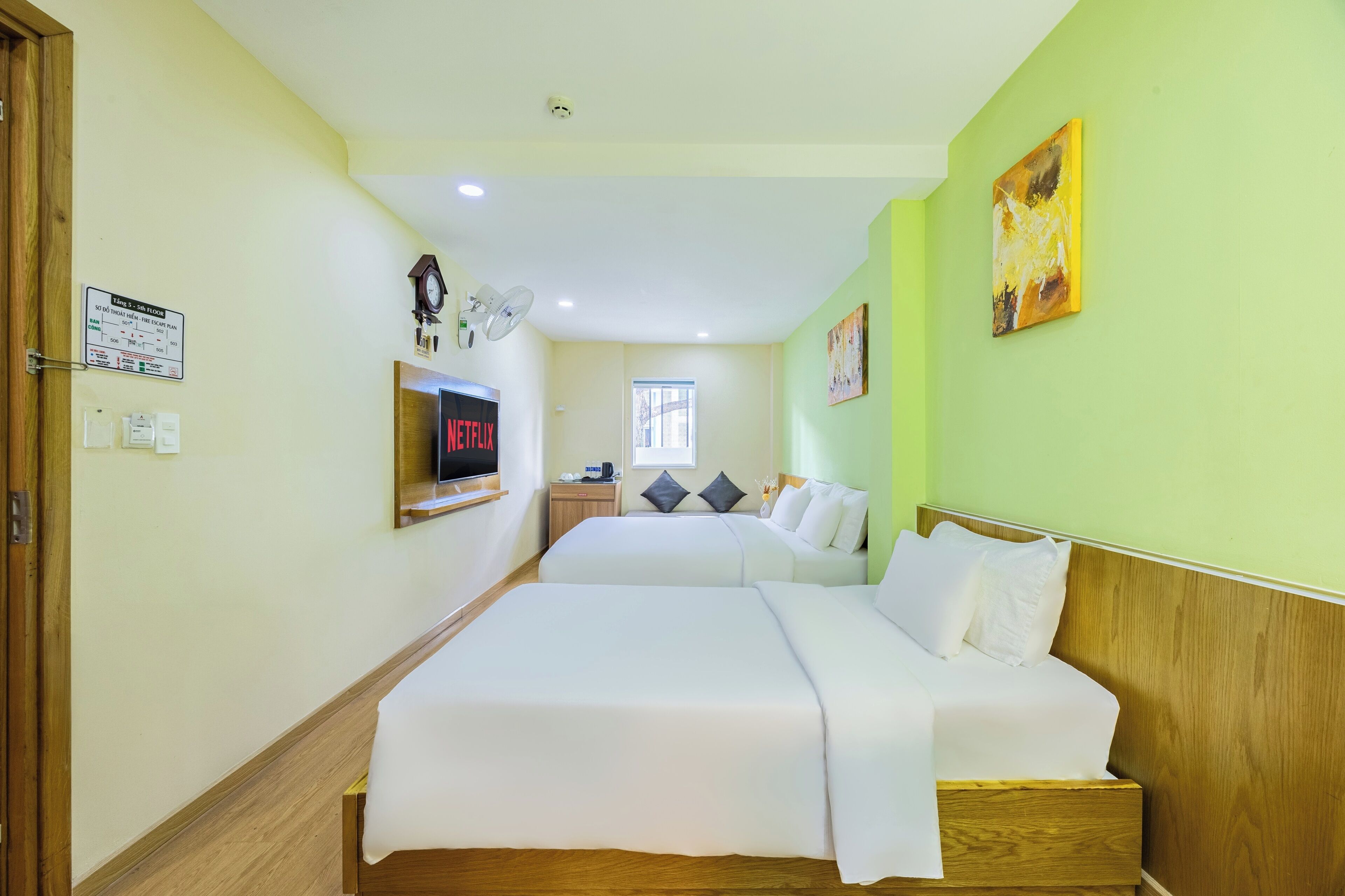 A hotel room with two beds, a clock, a TV, and a window.