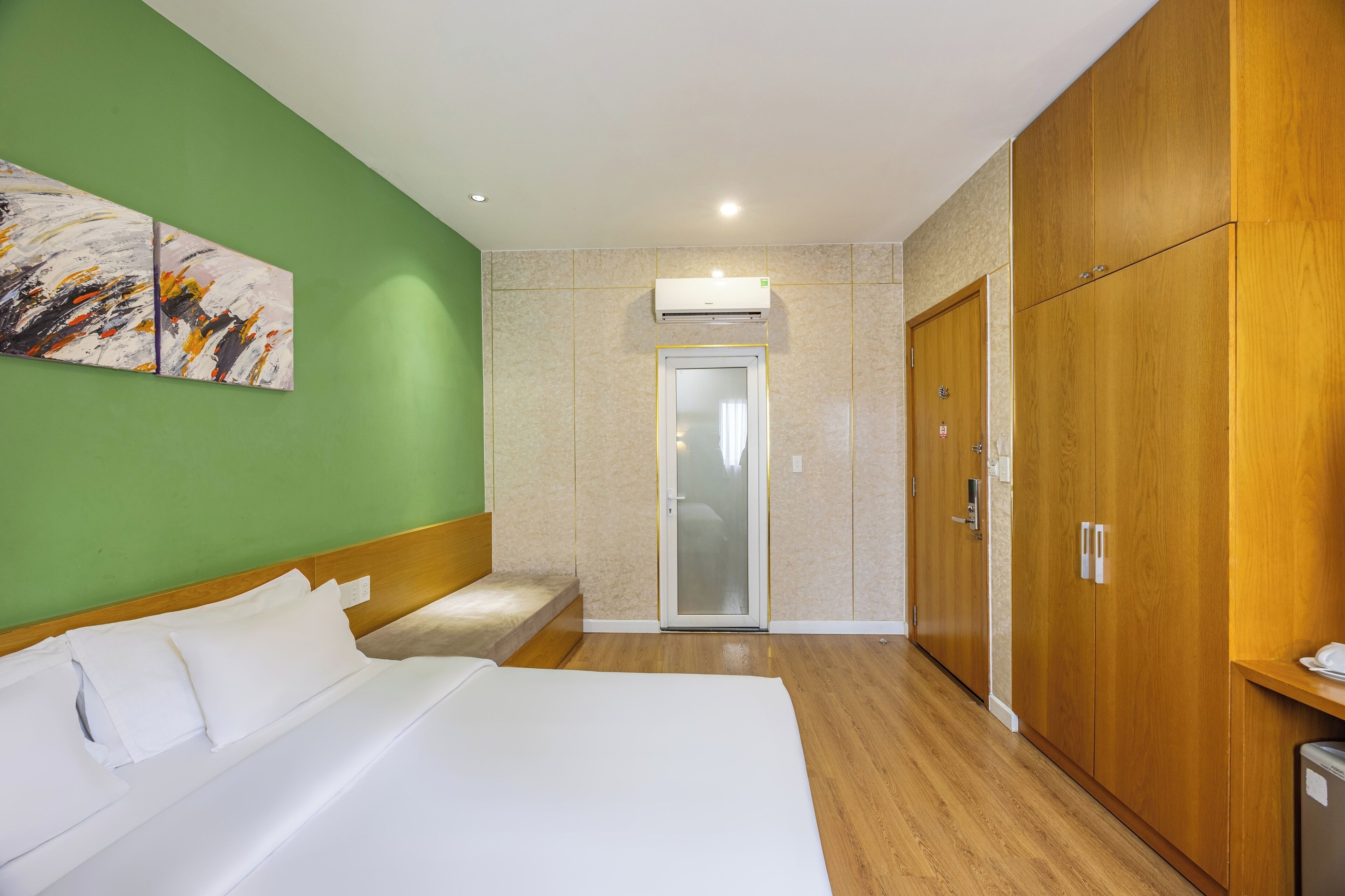 A hotel room with a bed, a wardrobe, a shower, and a green wall with artwork.