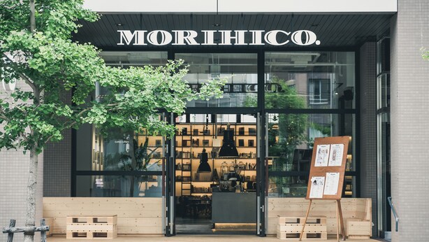 A storefront with a large glass window, a wooden bench outside, and a sign that reads "MORIHICO."