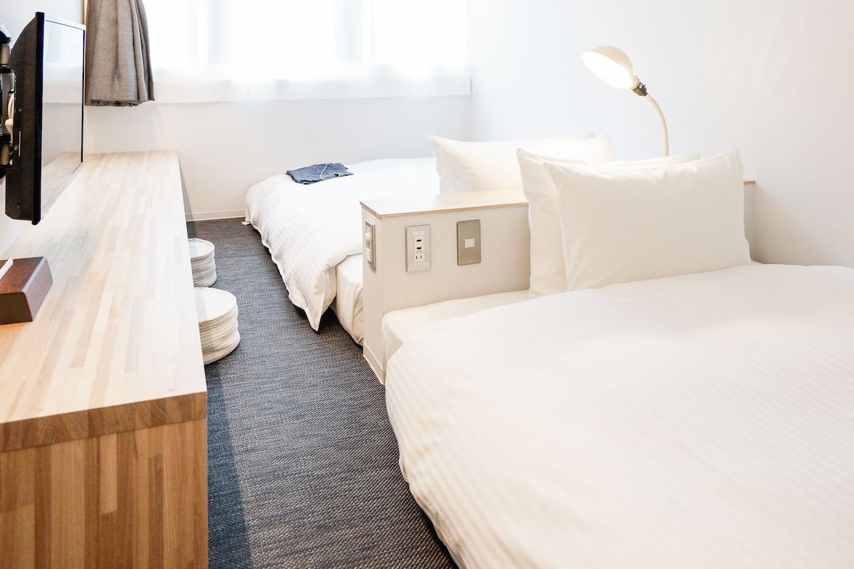 A hotel room with a wooden desk, a bed, a small table, and a window with curtains.