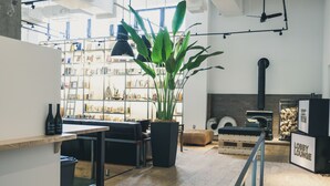 A modern lobby with a wooden floor, a black sofa, a large potted plant, and a bookshelf filled with books and decorative items.