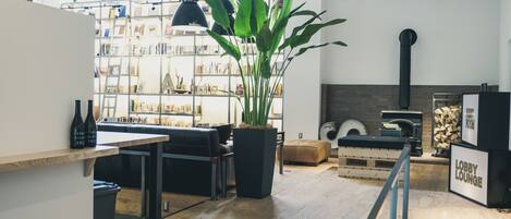 A modern lobby with a wooden floor, a black sofa, a large potted plant, and a bookshelf filled with books and decorative items.