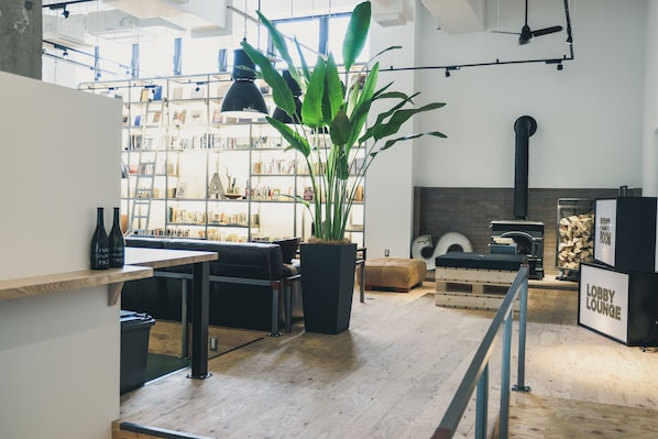 A modern lobby with a wooden floor, a black sofa, a large potted plant, and a bookshelf filled with books and decorative items.