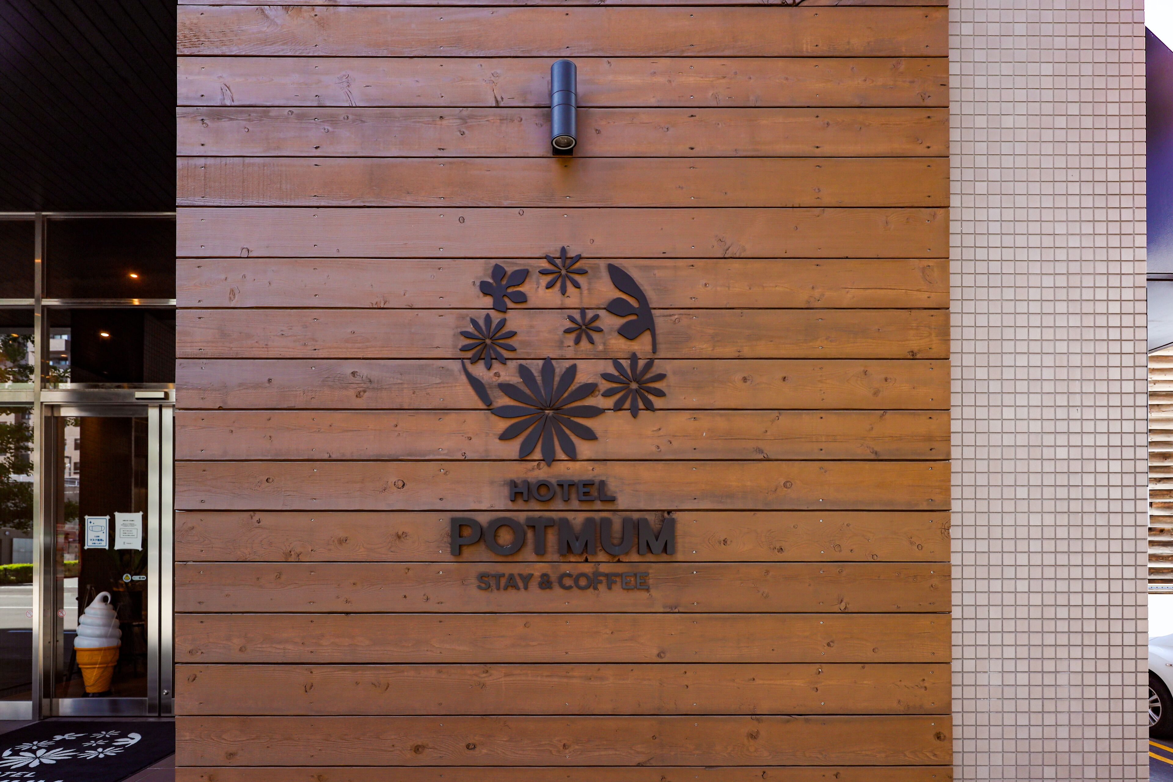 Pared de madera con un letrero del Hotel Potmum, Estancia y Café, y una cámara de seguridad sobre la entrada.