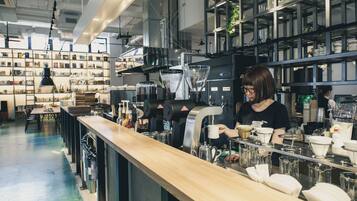 Interior de una cafetería con una barra larga, máquinas de café y estantes con diversos artículos.