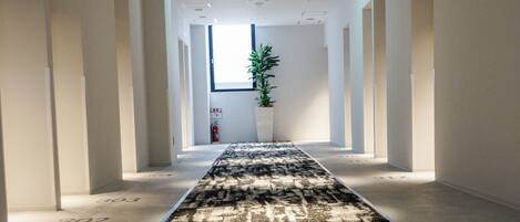 Un pasillo con alfombra estampada, paredes blancas y una planta en maceta.