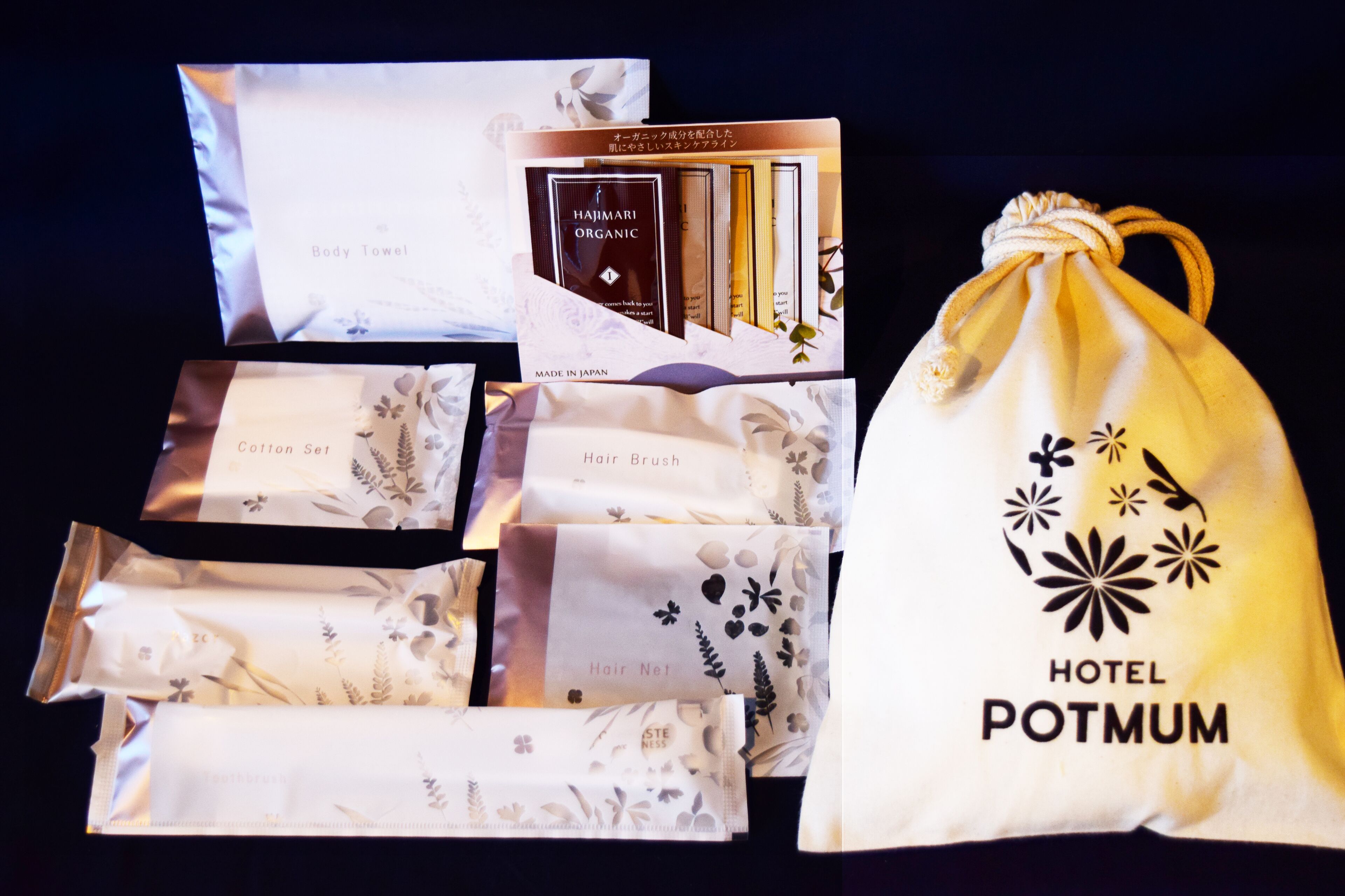 Un surtido de artículos de aseo que incluye una toalla de baño, juego de algodón, cepillo para el cabello, gorro de pelo y una bolsa con cordón que muestra el logotipo del Hotel Potmum.