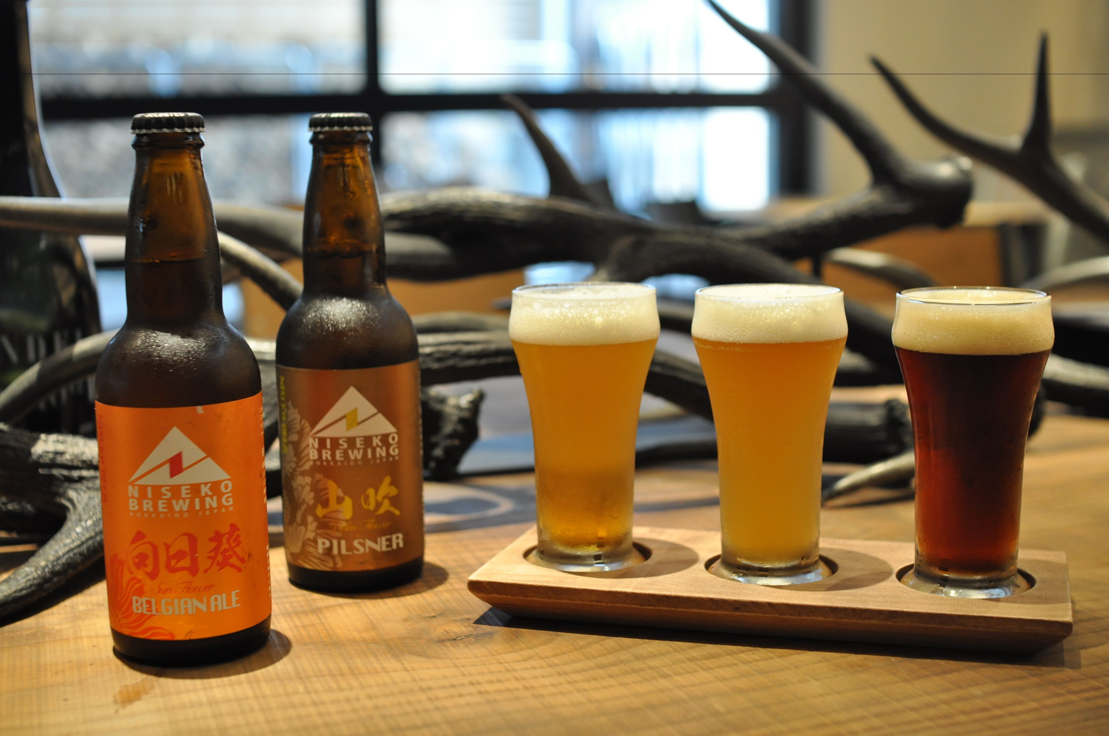 A wooden tray with four glasses of beer and two bottles of beer on a table.