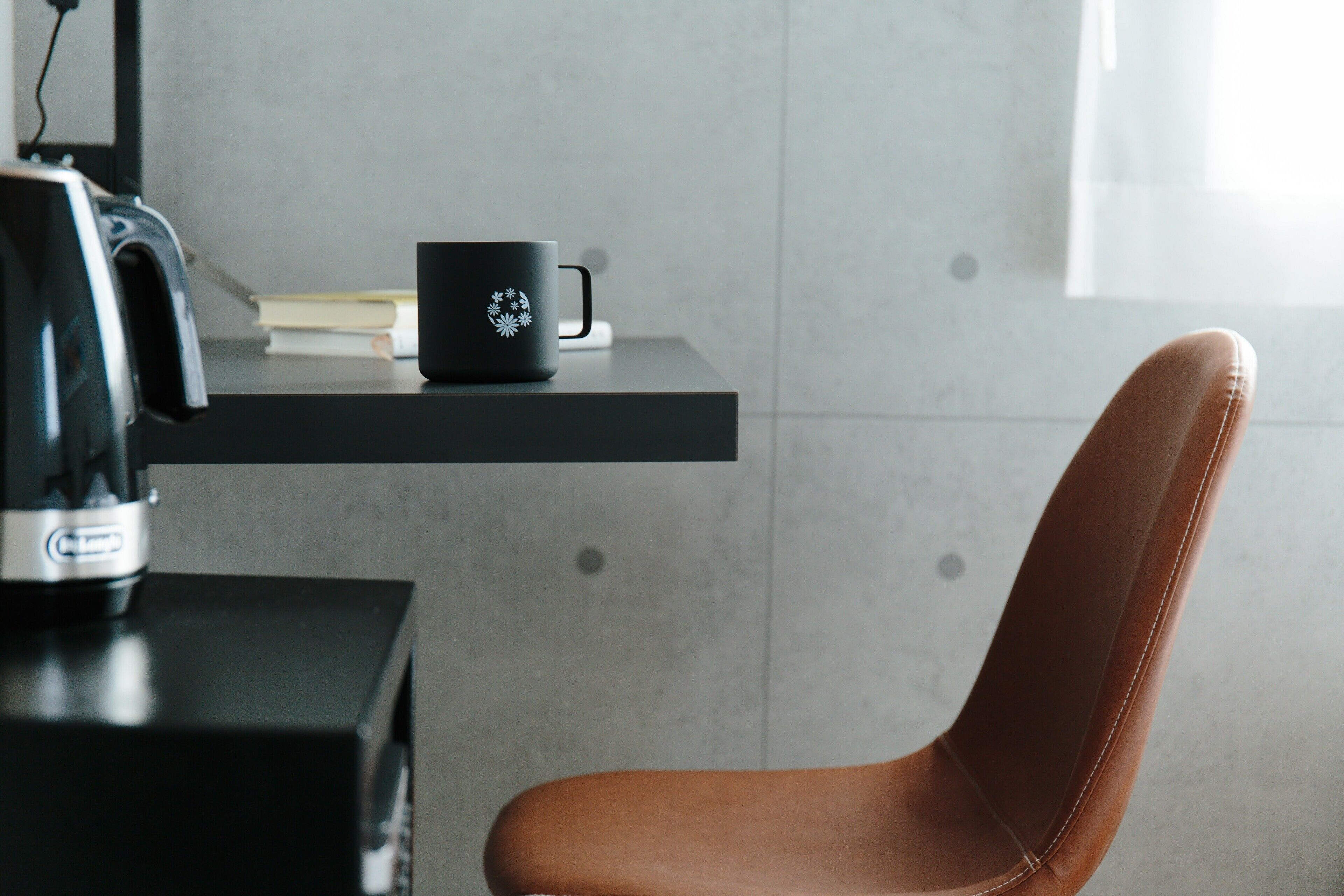 A modern room with a black coffee maker, a black mug with a floral design, and a brown leather chair.
