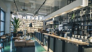 A modern coffee shop with a long counter, bookshelves, and a coffee station.