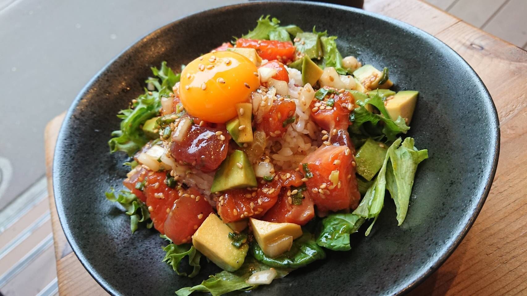Ensalada con aguacate, tomates y un huevo duro, sobre un plato oscuro.