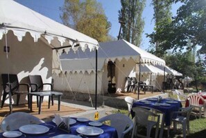 A row of white tents with tables set up for dining, surrounded by trees. - Royal Deluxe Camp (Leh)