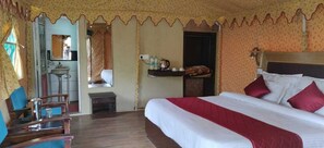 A hotel room with a large bed, a desk with a chair, a small table, and a mirror. - Royal Deluxe Camp (Leh)