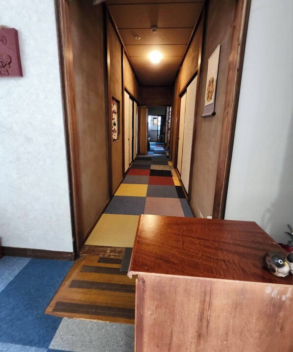 A hallway with a checkered carpet, wooden walls, and a wooden desk in the foreground. - Guest House Face to Face (Fujinomiya)