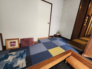 A hallway with a checkered carpet, a wooden bench, a small table with a plant, and a framed picture on the wall. - Guest House Face to Face (Fujinomiya)